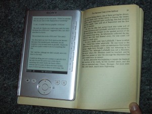 A Sony PRS pocket (PRS-300) digital reader on top of an open paperback book.